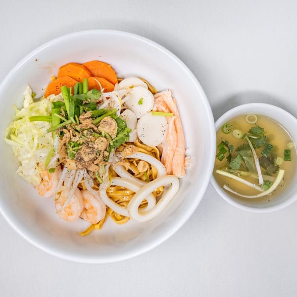 Vietnamese dry egg noodles with shrimp, squid, fish cakes, and vegetables, served with a side of broth.