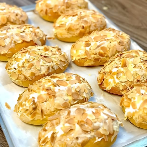 Rows of golden-brown Vietnamese pastries topped with white frosting and sliced almonds on a baking sheet.
