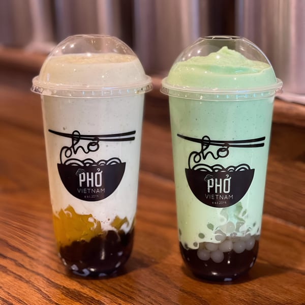 Two Pho Vietnam bubble tea drinks, one mango and one green, on a wooden table.