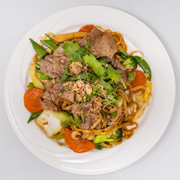 Vietnamese stir-fried noodles with beef, broccoli, carrots, baby corn, and snow peas, garnished with cilantro.