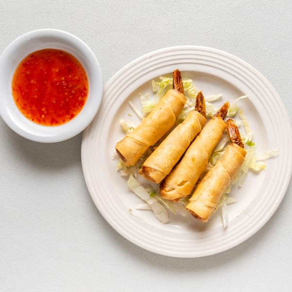 Four golden-fried shrimp spring rolls on shredded lettuce, with a side of red chili dipping sauce.