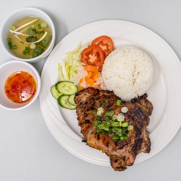 Vietnamese grilled pork chop with rice, salad, and two small bowls of soup and chili sauce.
