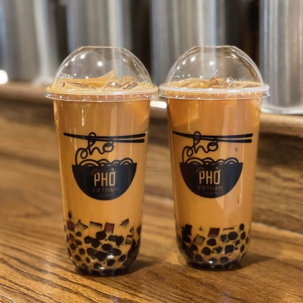 Two Pho Vietnam bubble teas with tapioca pearls and ice on a wooden table.