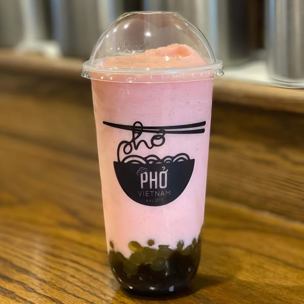 Pink Pho Vietnam bubble tea with dark tapioca pearls on a wooden surface.