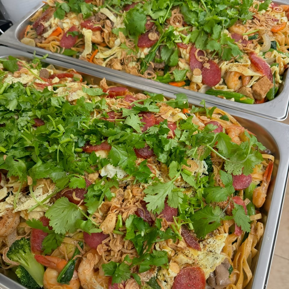 Two large trays of Vietnamese stir-fried noodles with shrimp, sausage, egg, and cilantro.