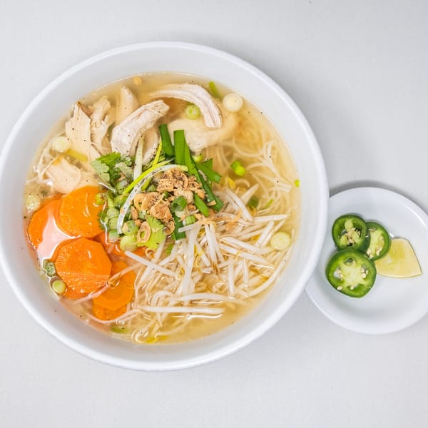 A bowl of Pho Vietnam chicken noodle soup with carrots, bean sprouts, and a side of jalapeños and lime.
